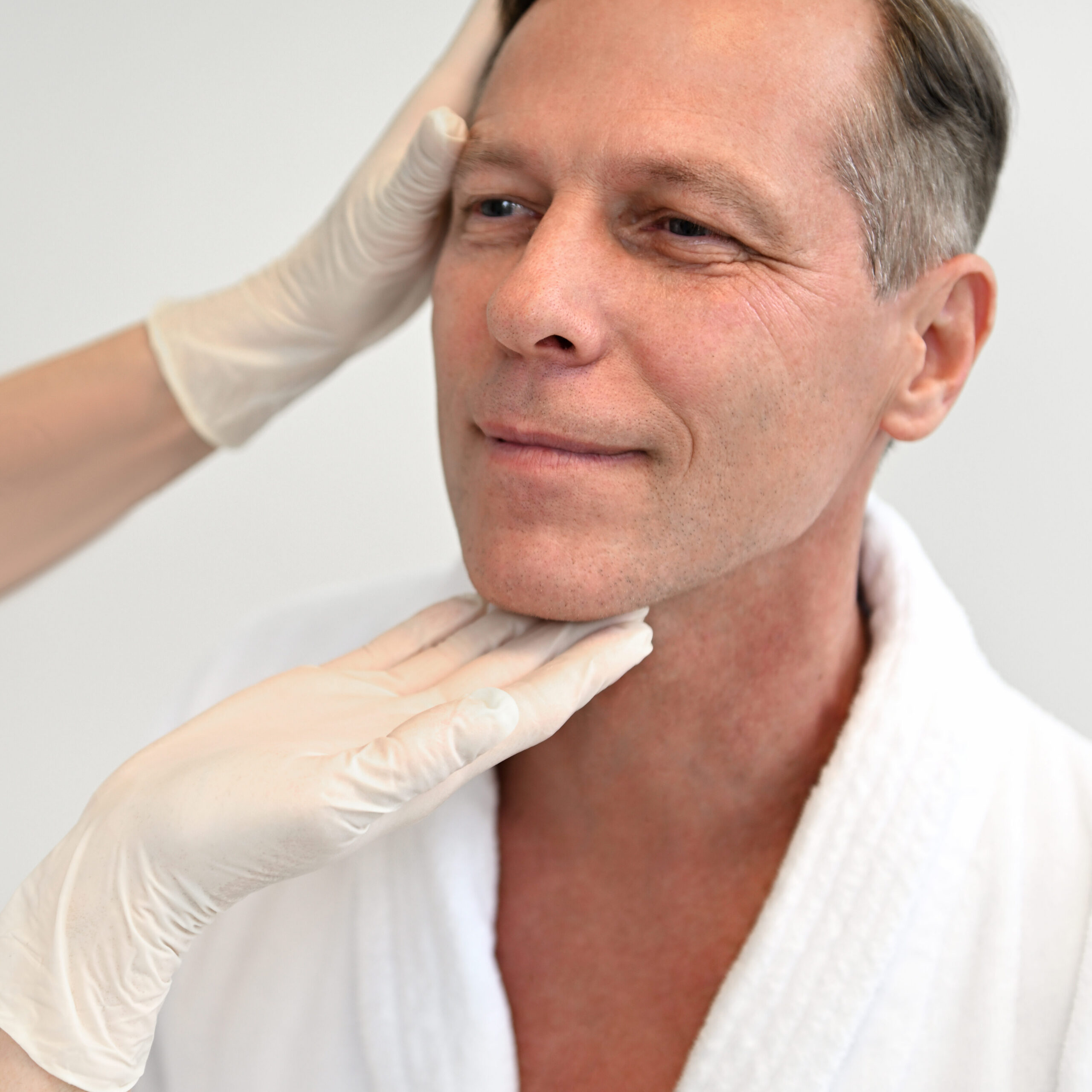 Close-up of a female doctor examining handsome mature European man in medical clinic. Physiotherapist doing facial manual massage to a middle aged patient at wellness spa center. Health care concept